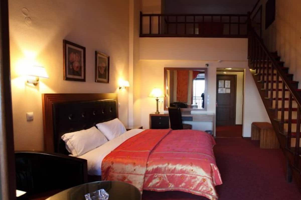 Une chambre d’hôtel comprenant un lit, des tables de chevet, une lampe, un escalier et une porte donnant sur une autre pièce.