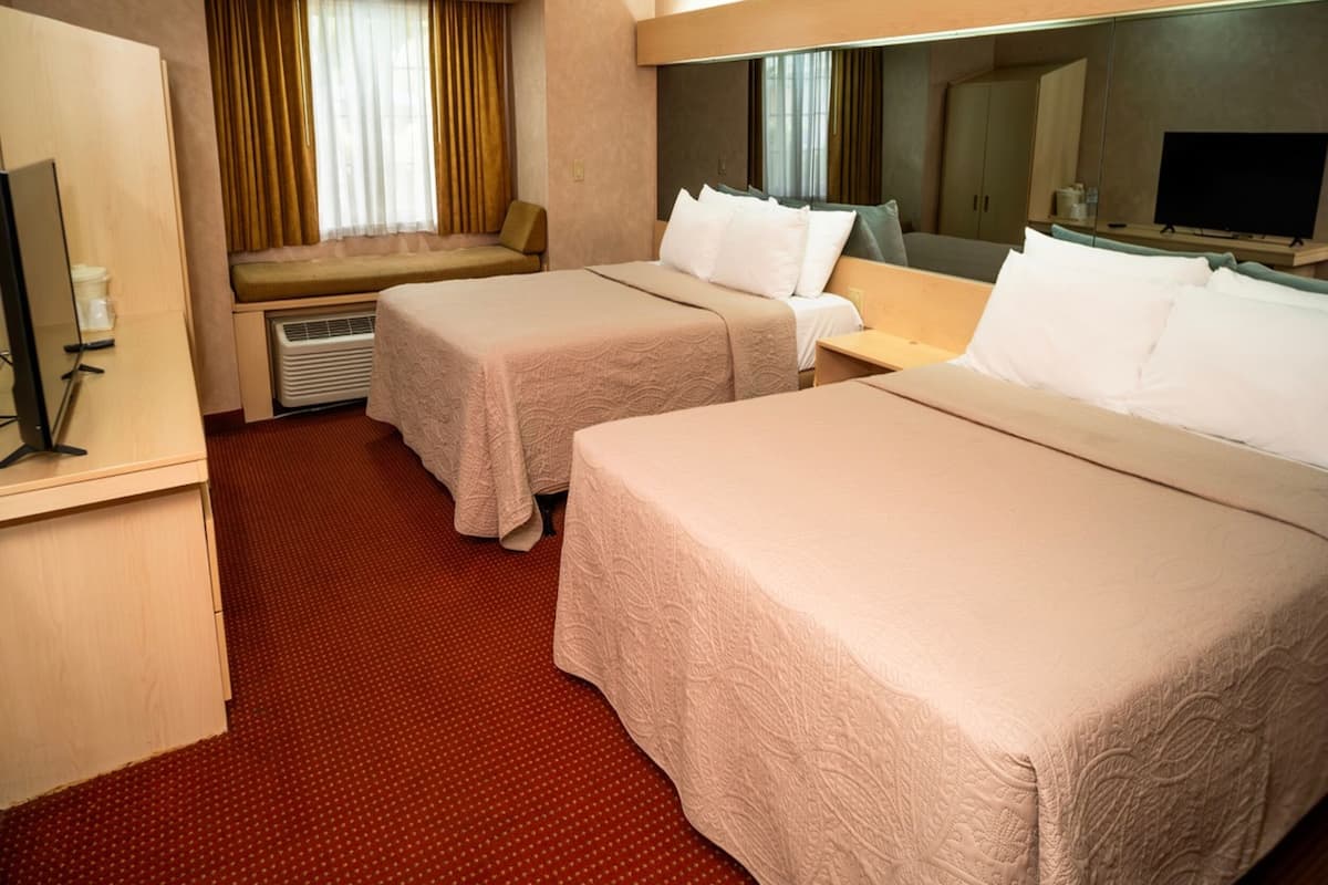 Habitación de hotel con dos camas, un escritorio, televisor y una ventana con cortinas.