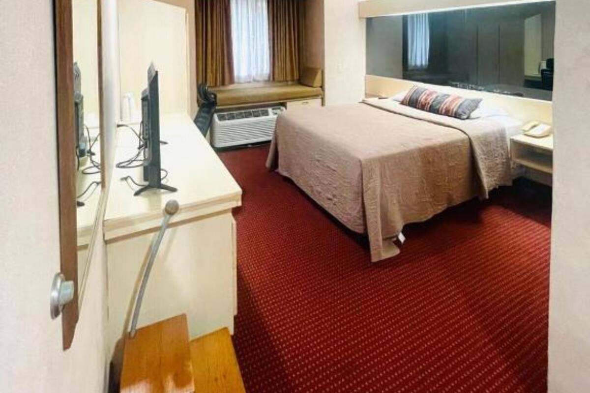 Habitación de hotel con cama, escritorio con computadora, espejo y ventana con cortinas.