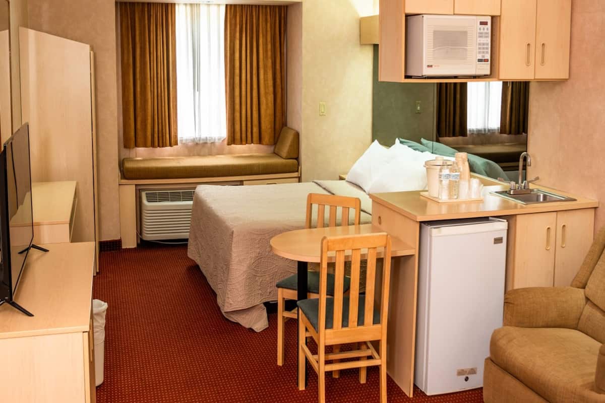 Habitación de hotel compacta con cama, una pequeña mesa de comedor con sillas, kitchenette con microondas y televisor.