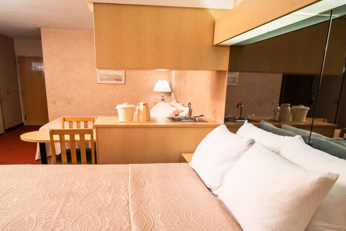 Una habitación de hotel con una cama grande, un escritorio con lámpara y una pequeña kitchenette.