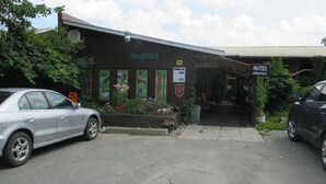 Un edificio con un letrero que dice "94 QUEEN" y "Motel Lennoxville". Hay dos coches estacionados adelante, un cantero con diversas plantas y una señal que indica zona de no estacionamiento.