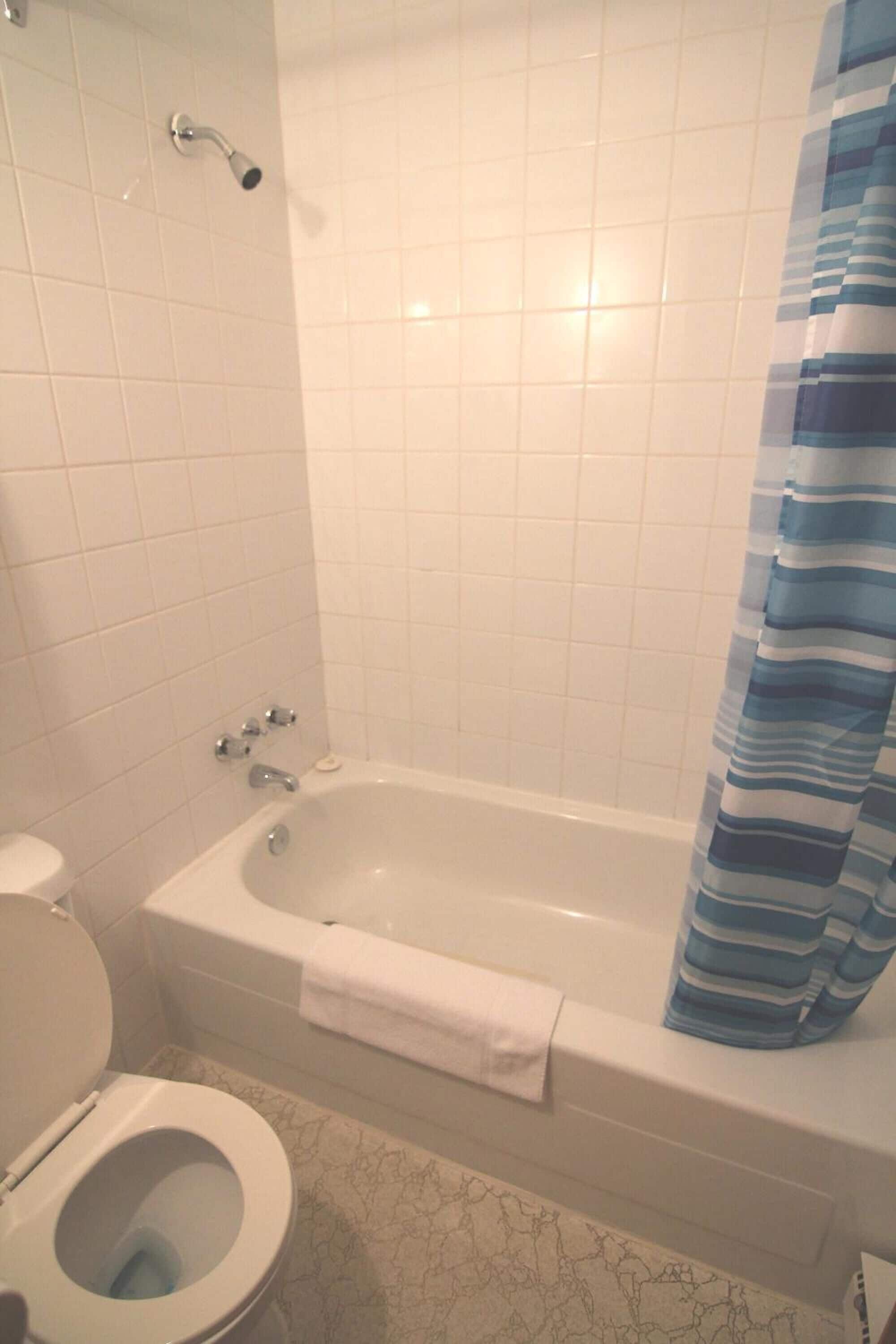 A bathroom with a white toilet, a bathtub with a blue-striped shower curtain, and a white towel on the tub.