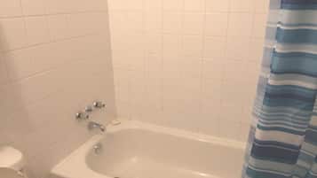 A bathroom with a white toilet, a bathtub with a blue-striped shower curtain, and a white towel on the tub.