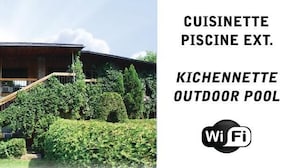 Un edificio de dos pisos con fachada de madera y un balcón. Tiene un letrero que indica 'CUISINETTE PISCINE EXT.' y 'KICHENNETTE OUTDOOR POOL'.