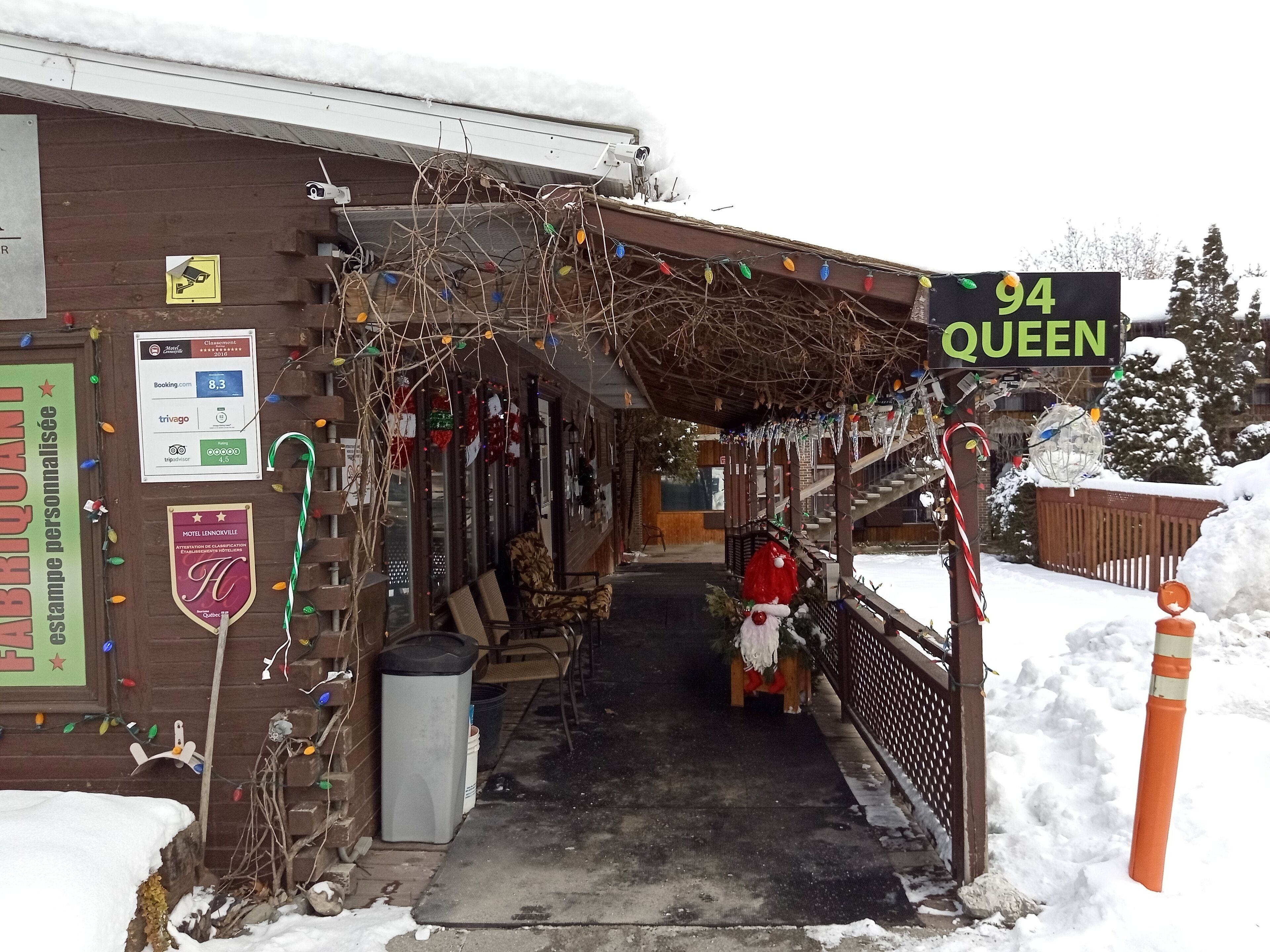 A snow-covered building with a sign reading "94 QUEEN" and a covered entrance area with seating and a trash bin.