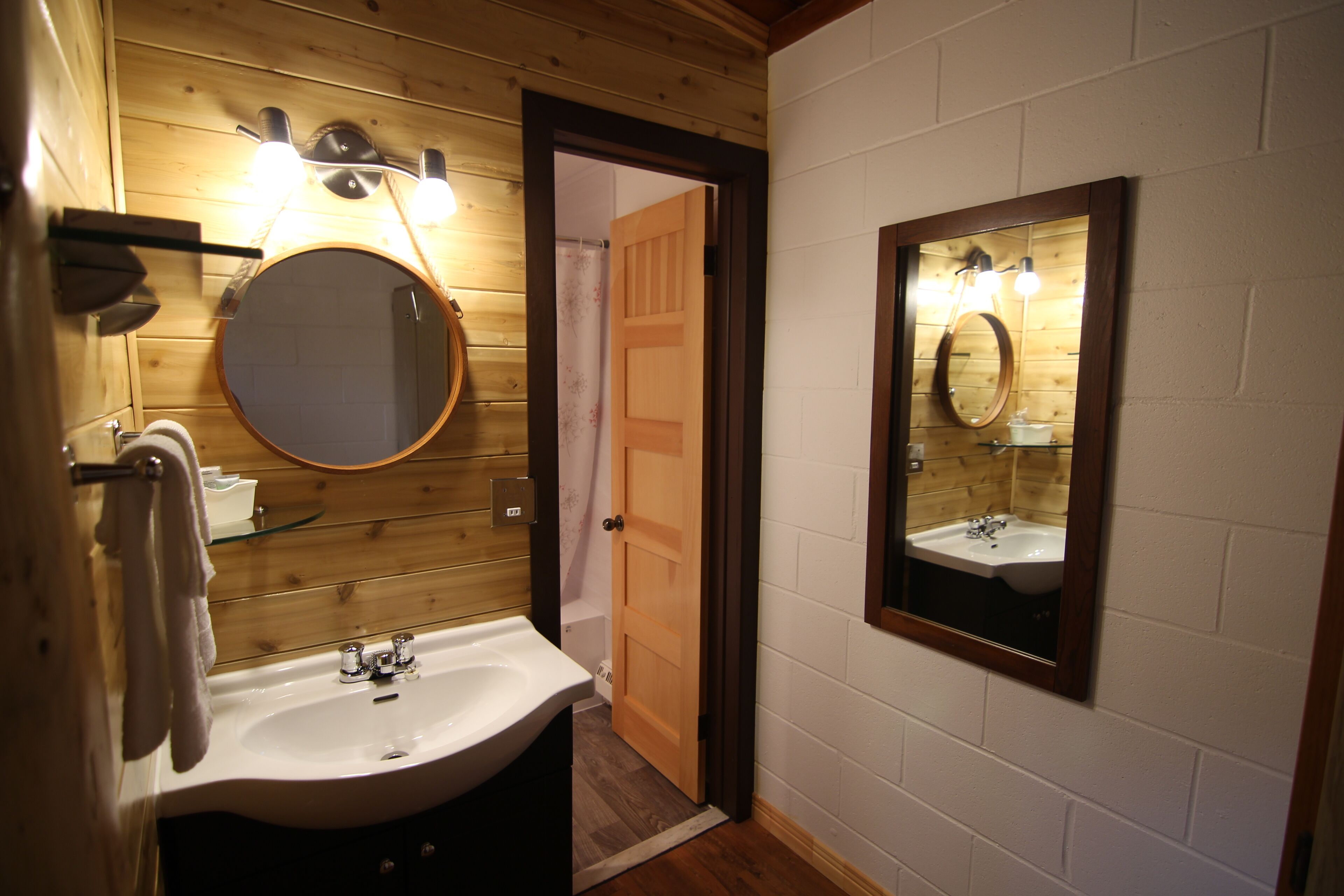 A bathroom with a wooden ceiling, a round mirror, a sink, and a door leading to another room.