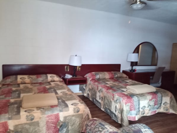 Una habitación de hotel con dos camas, un escritorio, una silla, una lámpara y un espejo.