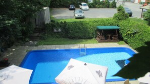 Piscina con escalera, rodeada de follaje y una terraza de madera.
