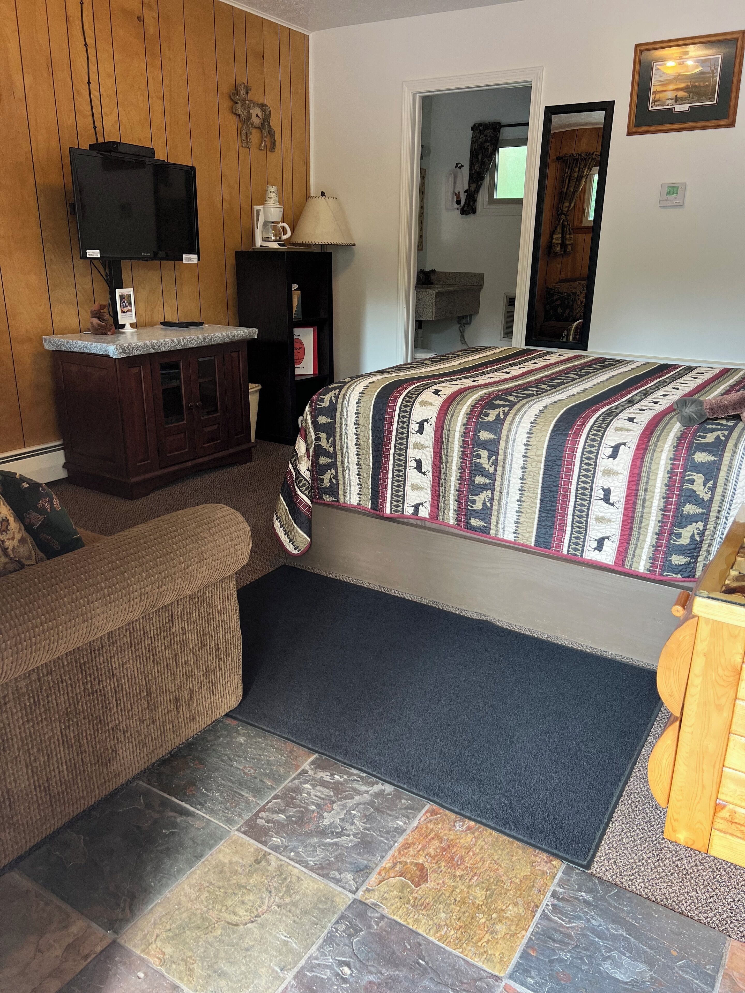 A cozy room with a bed, a wooden cabinet, a television, and a coffee maker.