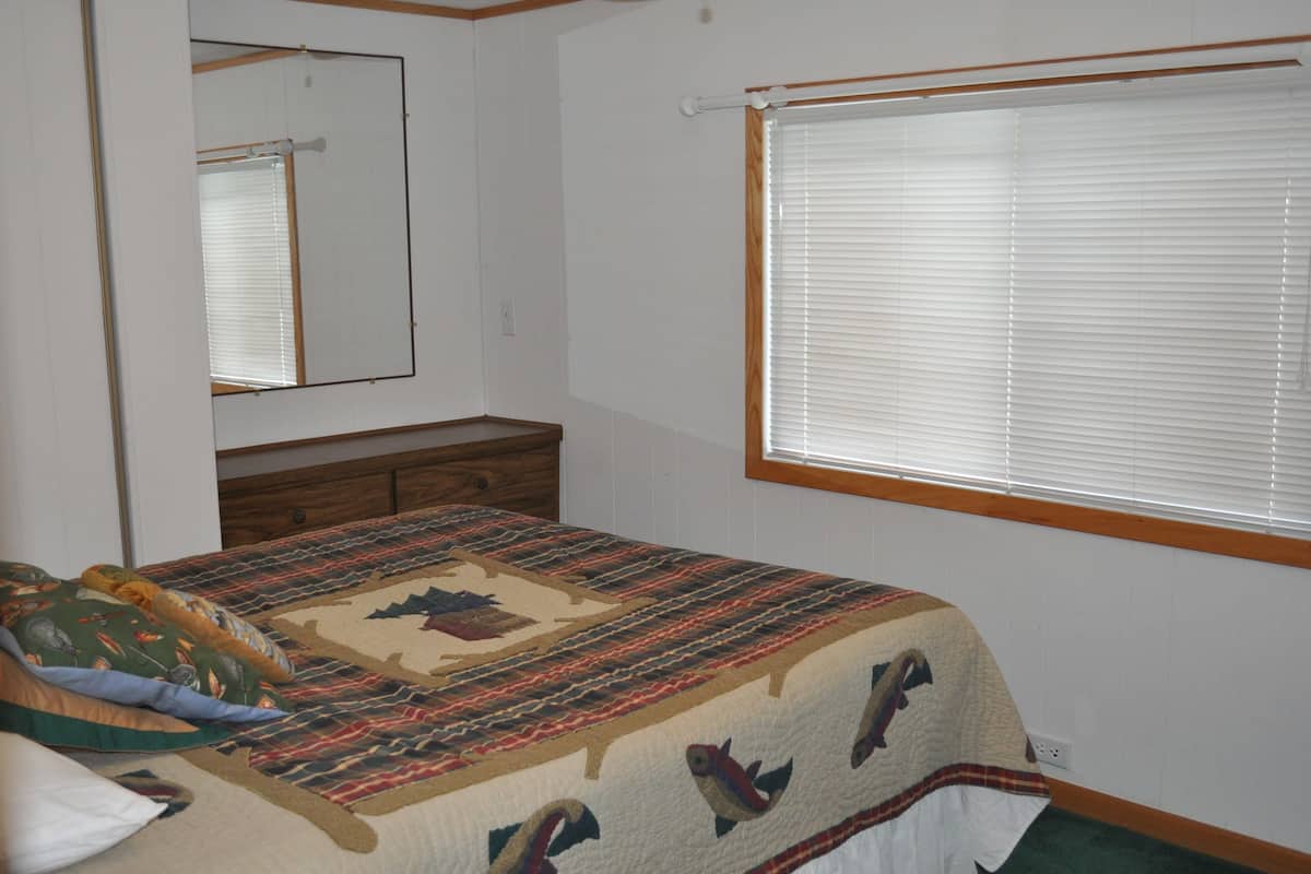 A bedroom with a bed, a dresser, a mirror, and a window with blinds.