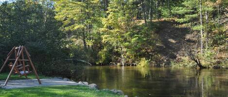 A wooden swing set near a pond surrounded by trees.