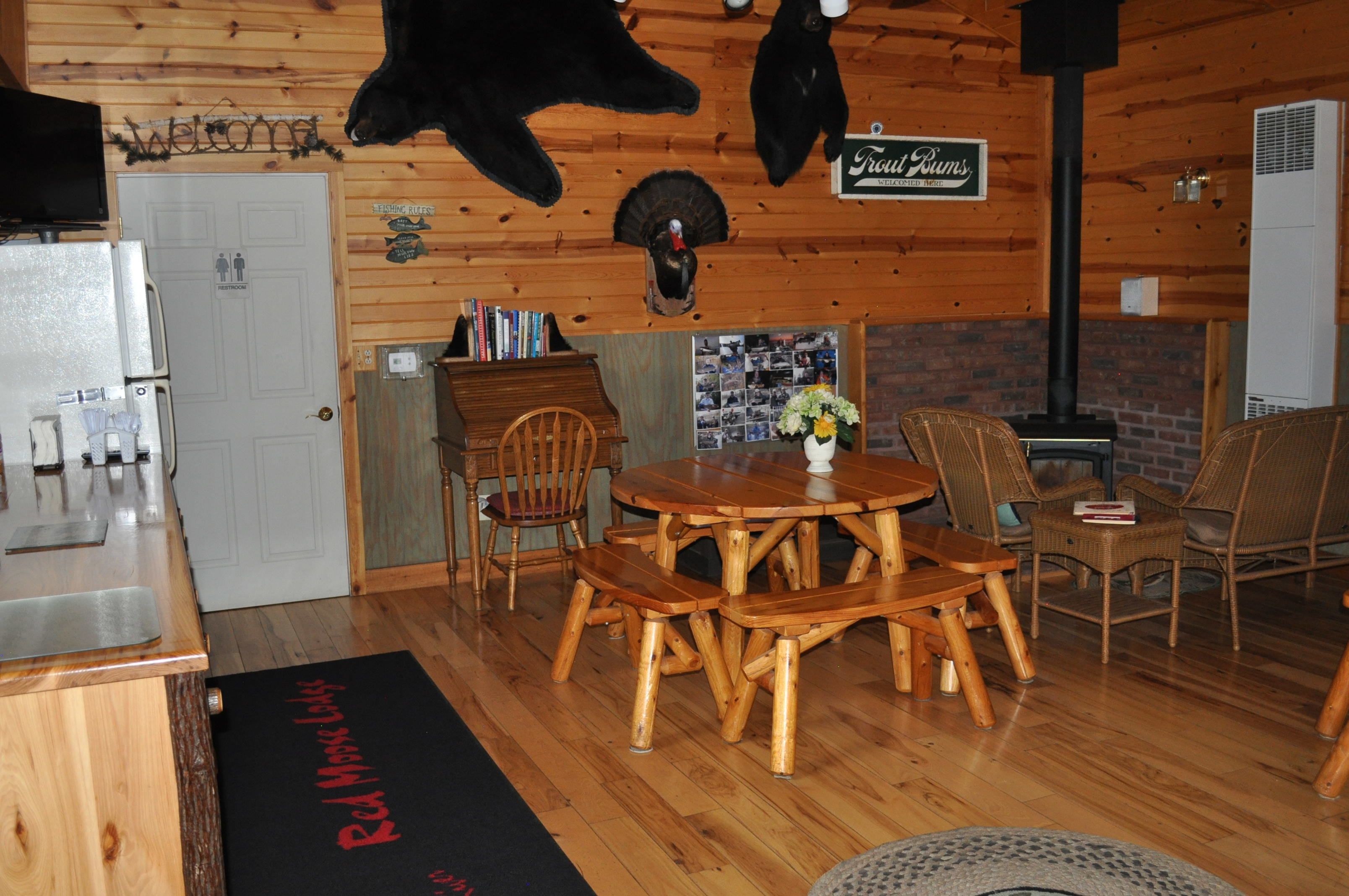 A wooden interior with a dining table, chairs, a fireplace, and a sign reading "Trouf Bums".