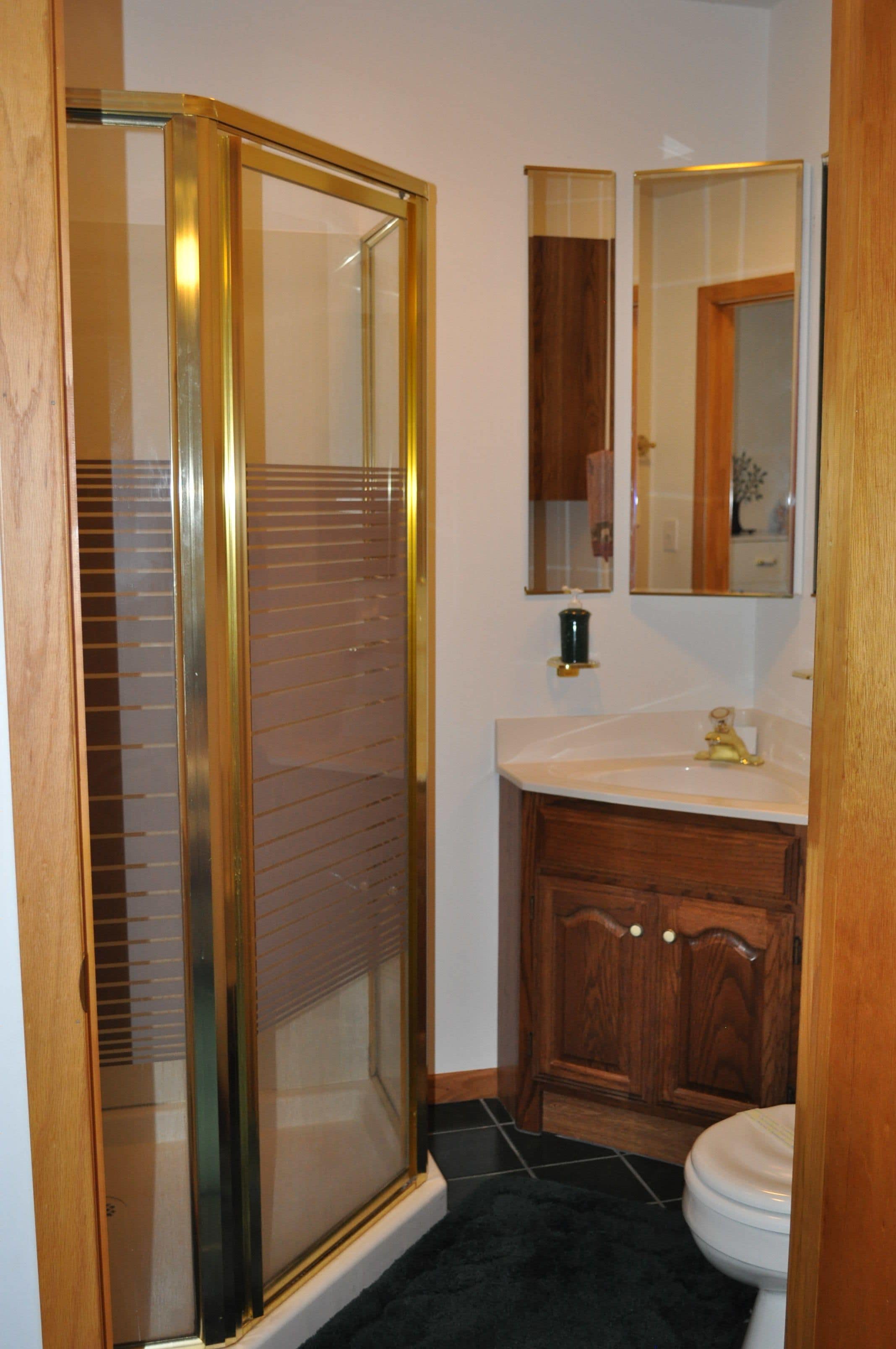 Un baño con cabina de ducha de vidrio, tocador de madera y espejo sobre el lavabo.