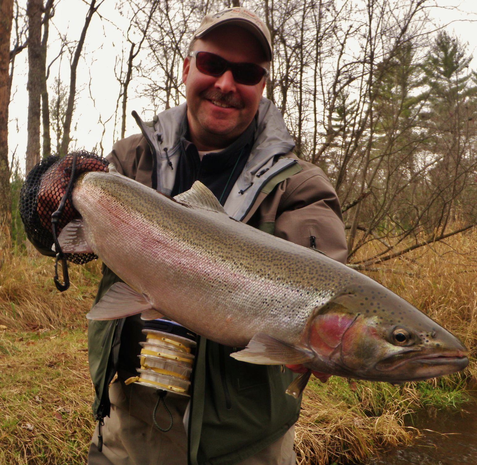 A person holding a large fish, wearing a jacket and a cap.