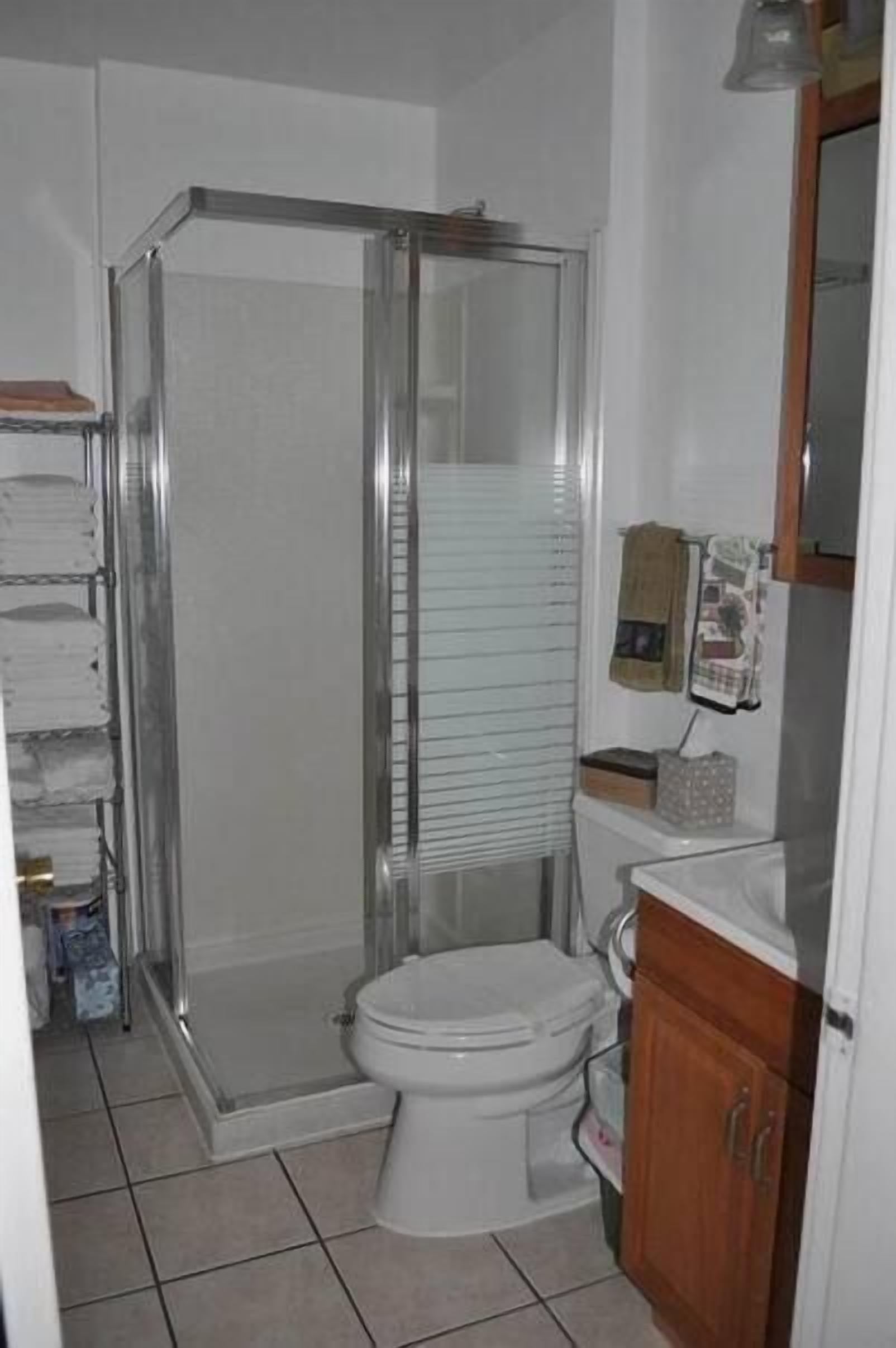 A bathroom with a glass-enclosed shower, a toilet, and a wooden cabinet.