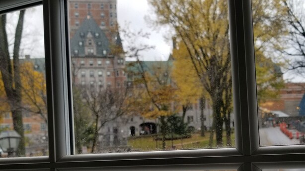 A window with a view of a building with a green roof and a brick facade. - Auberge du Tresor (Québec City)