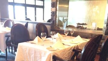 Un restaurante con pared de piedra, suelo de madera y mesas dispuestas con manteles blancos y copas de vino.