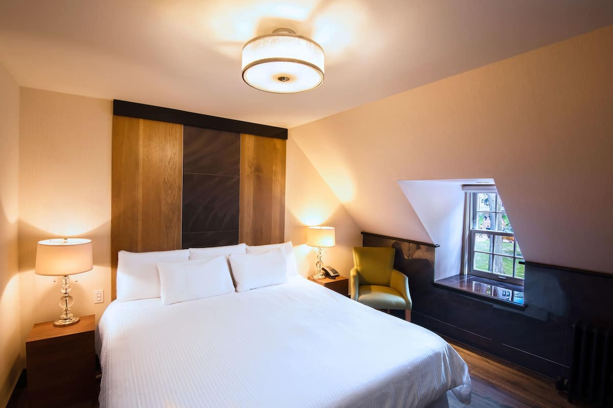 A hotel room with a large bed, two bedside lamps, a chair, and a window with a view.