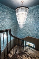 Una escalera con barandilla de madera, un candelabro y papel tapiz estampado.