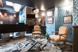 Una habitación con una mesa de centro de vidrio, dos sillas de mimbre, un aparador de madera oscura y papel tapiz estampado.
