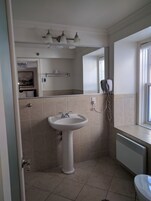 A bathroom with a pedestal sink, a mirror, a hairdryer, and a window.