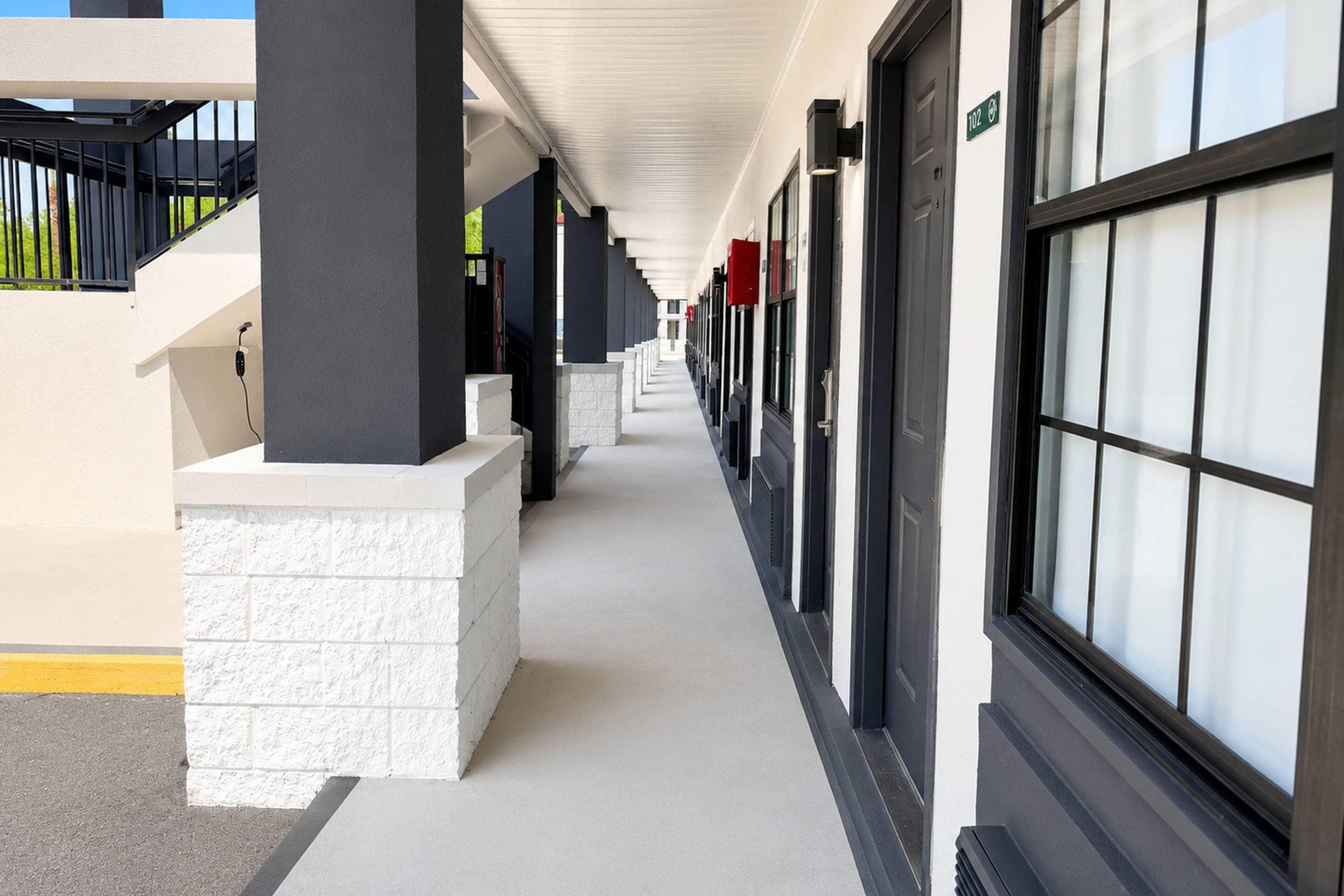 Un couloir bordé de fenêtres et de portes, avec une base en briques blanches et une rambarde noire sur le côté gauche.