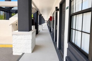 A corridor with a series of windows and doors, a white brick base, and a black railing on the left.