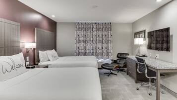 A hotel room with two beds, a desk, a chair, a lamp, and a patterned curtain.