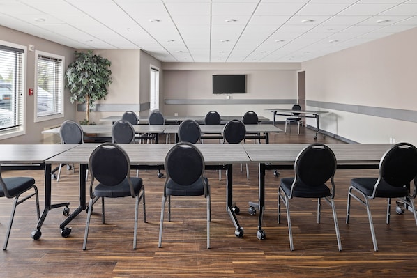 Un salón de conferencias con una larga mesa, varias sillas, una planta grande y un televisor de pantalla plana en la pared.