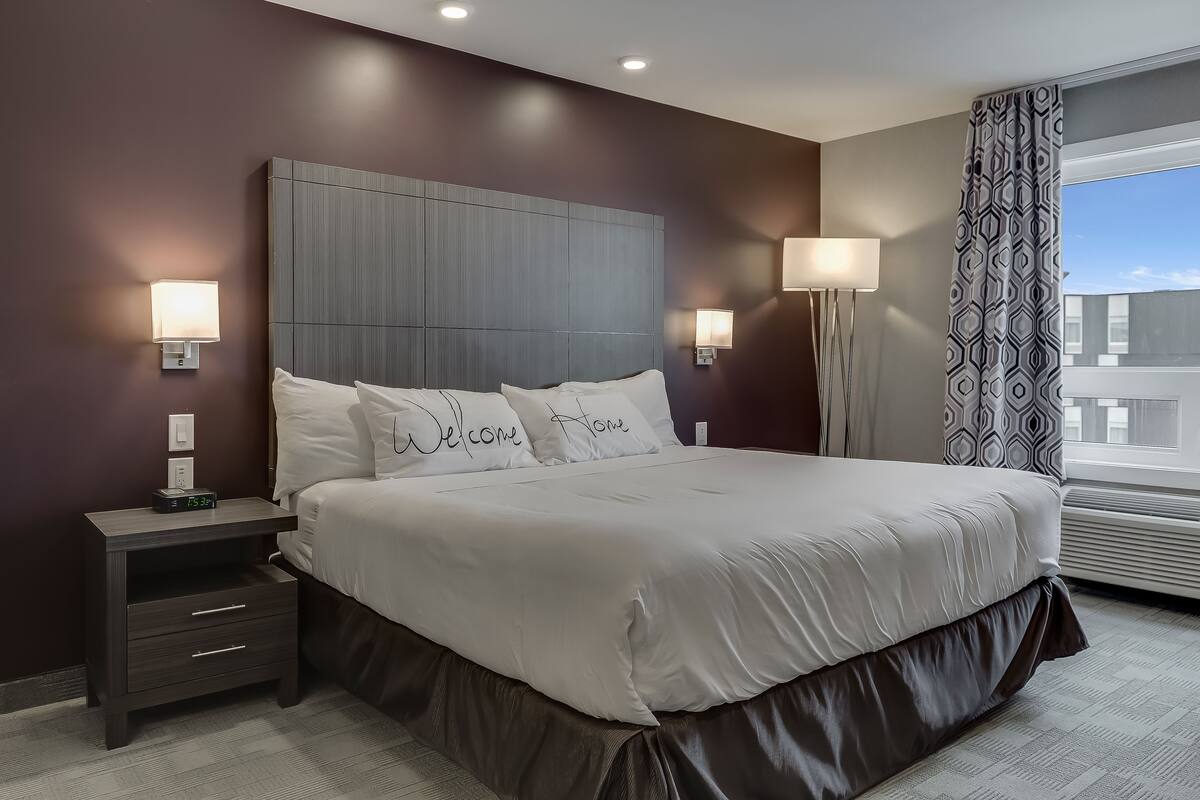 Une chambre moderne avec un grand lit, des lampes de chevet, une table de nuit et une fenêtre agrémentée de rideaux à motifs.