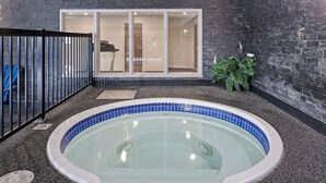 Un jacuzzi con borde de azulejos azules, cerca de una valla metálica negra y una planta en maceta junto a un muro de piedra oscura.