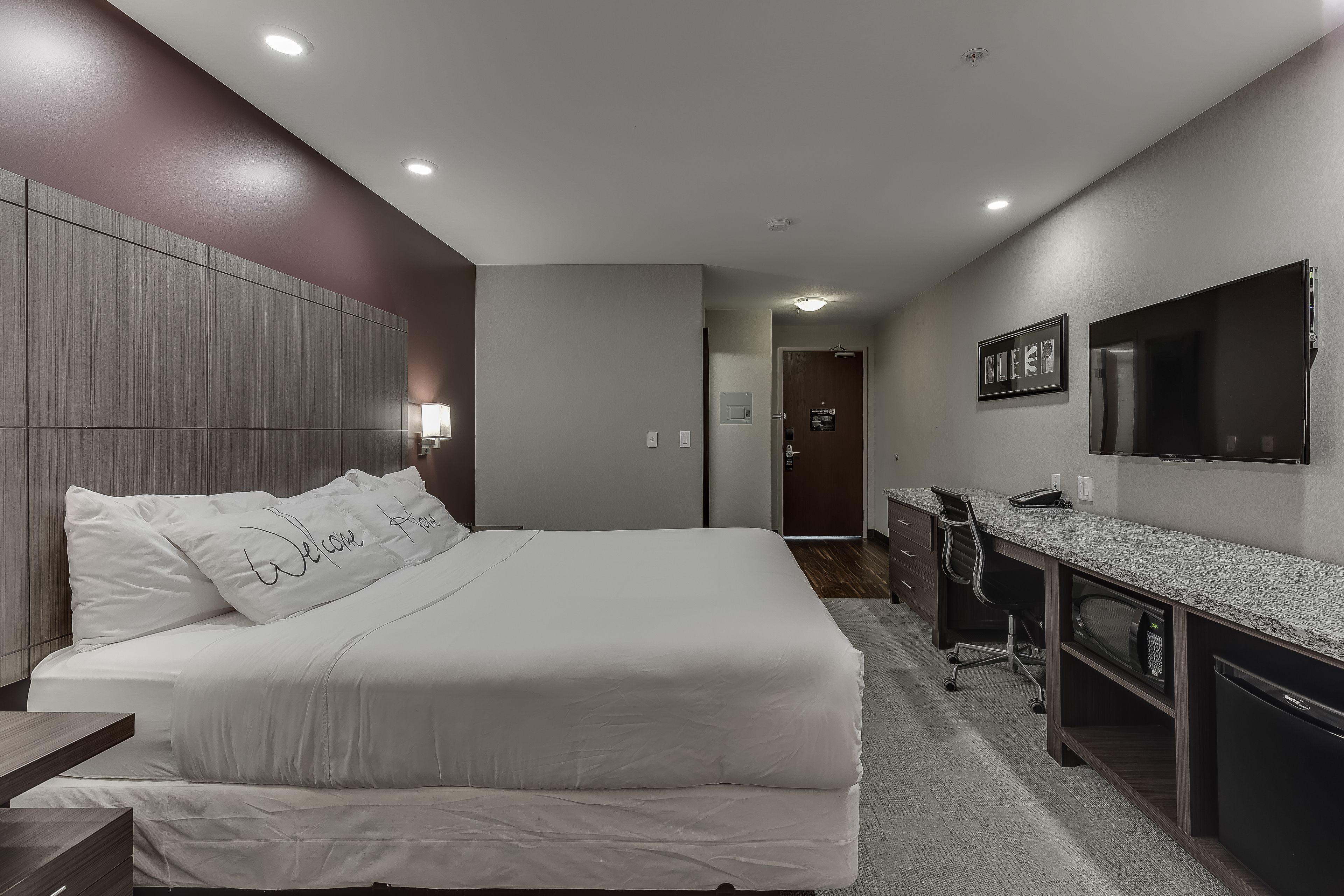 A hotel room with a large bed, a desk, a chair, and a television on the wall.