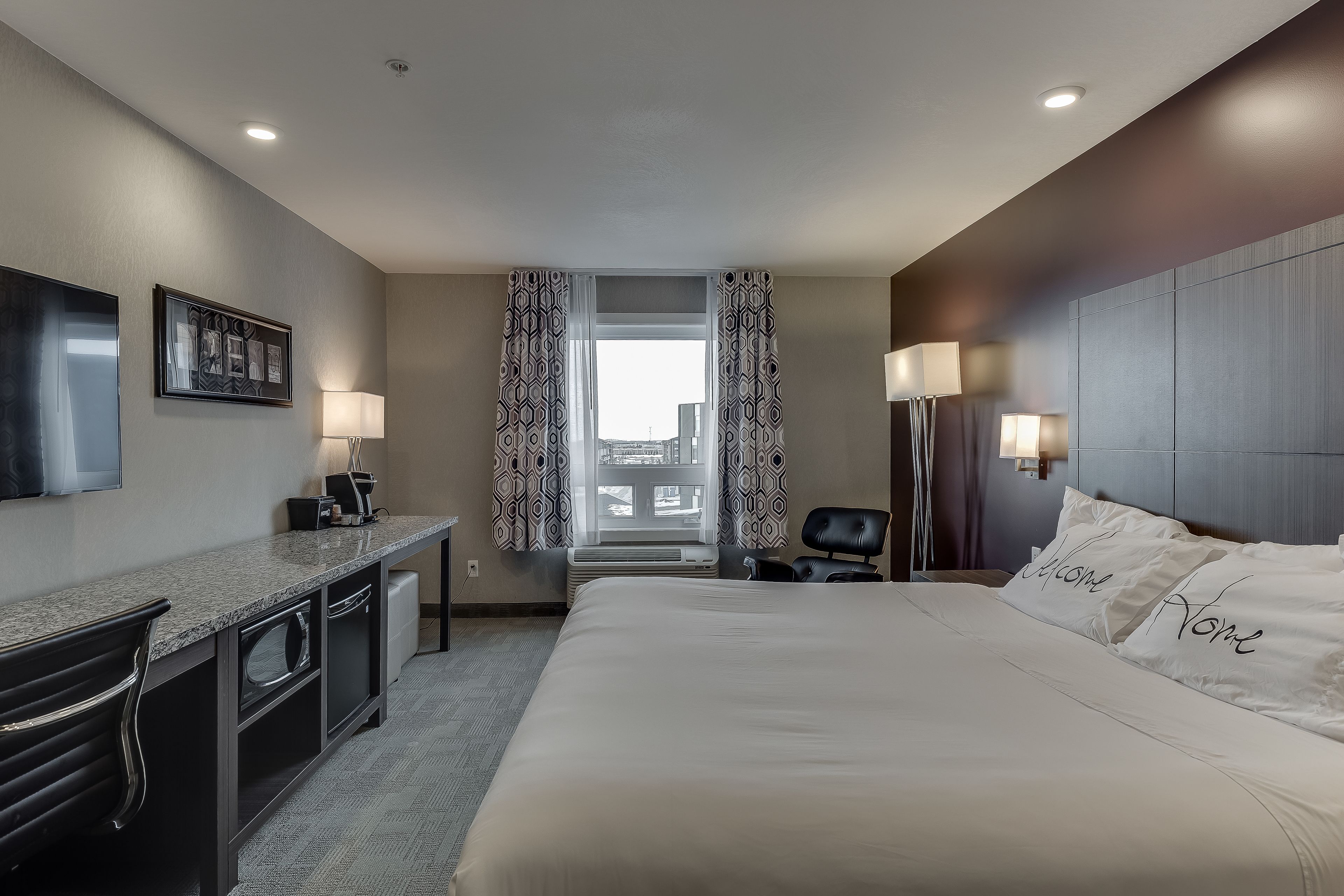 Habitación de hotel con cama, escritorio, silla y vistas de la ciudad a través de la ventana.