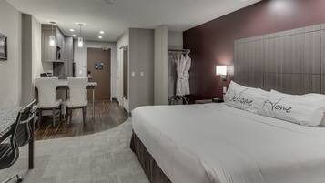 Een moderne hotelkamer met een groot bed, een bureau met stoelen, een kledingrek en een zichtbare badkamer door een geopende deur.