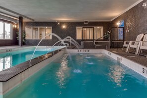 Une piscine intérieure à l’eau claire, avec des repères indiquant la profondeur et un mur en pierre en arrière-plan.