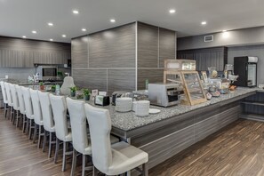 Une cuisine moderne dotée d’un long comptoir, de tabourets de bar blancs et d’un four encastré.