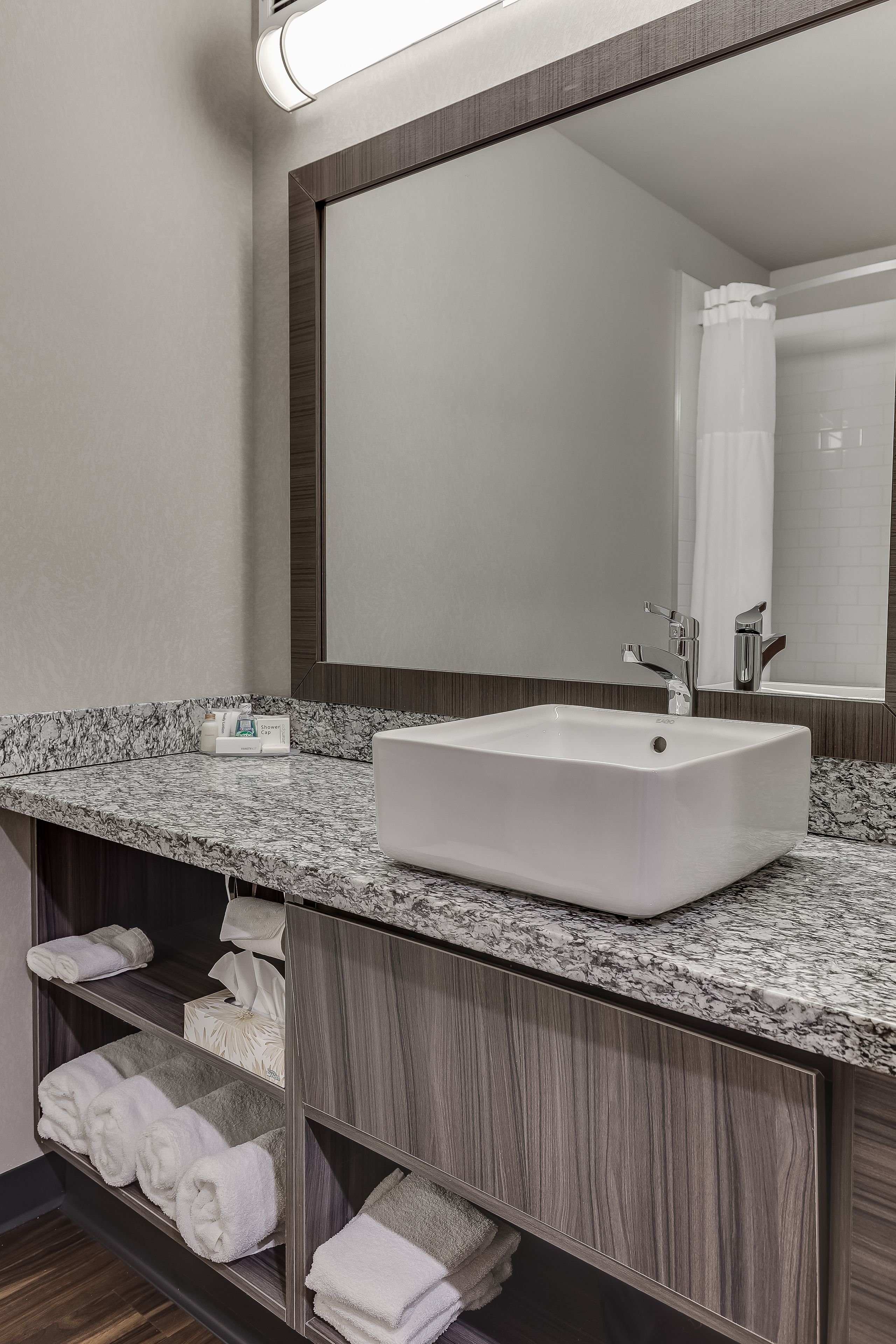 A bathroom with a large mirror, a white sink, and shelves with towels.
