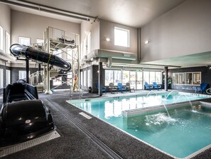 An indoor swimming pool with a water slide, lounge chairs, and a view of the street outside. - Home Inn & Suites Saskatoon South (Saskatoon)
