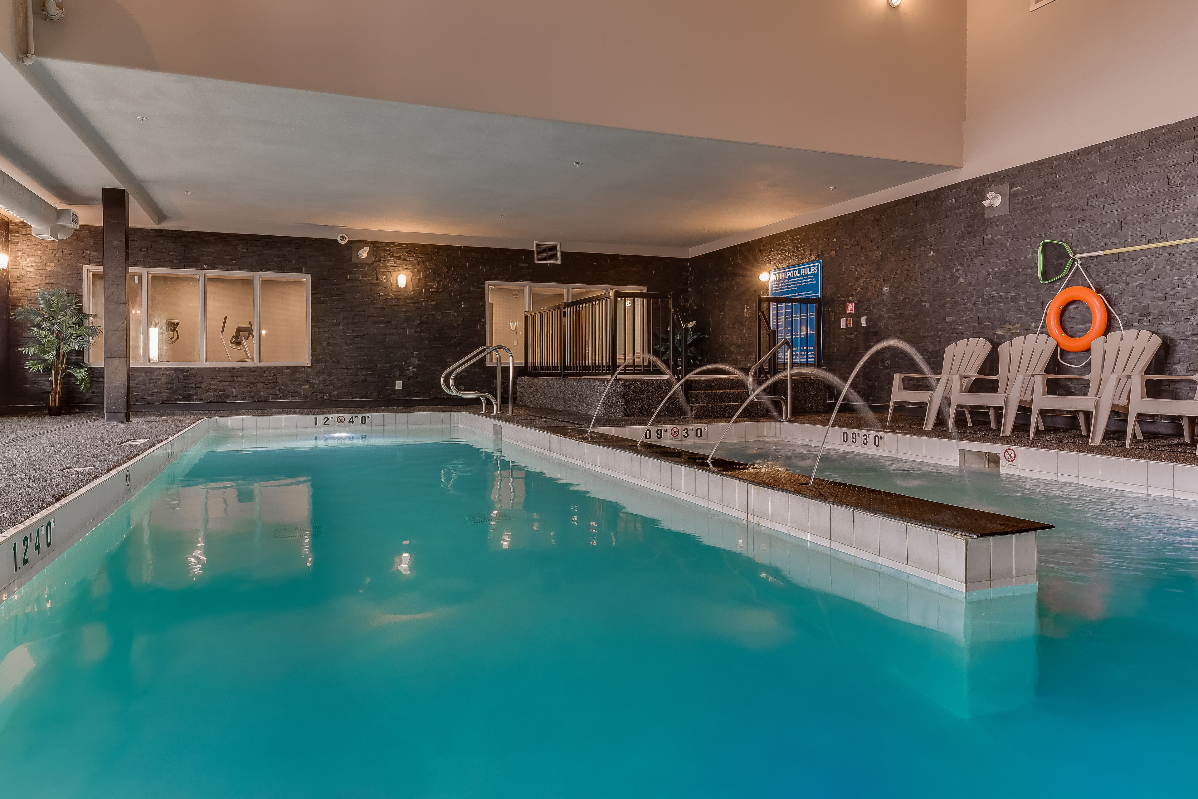 Una piscina interior con agua cristalina, un vestuario y un área de descanso con sillas y una mesa junto a la piscina.