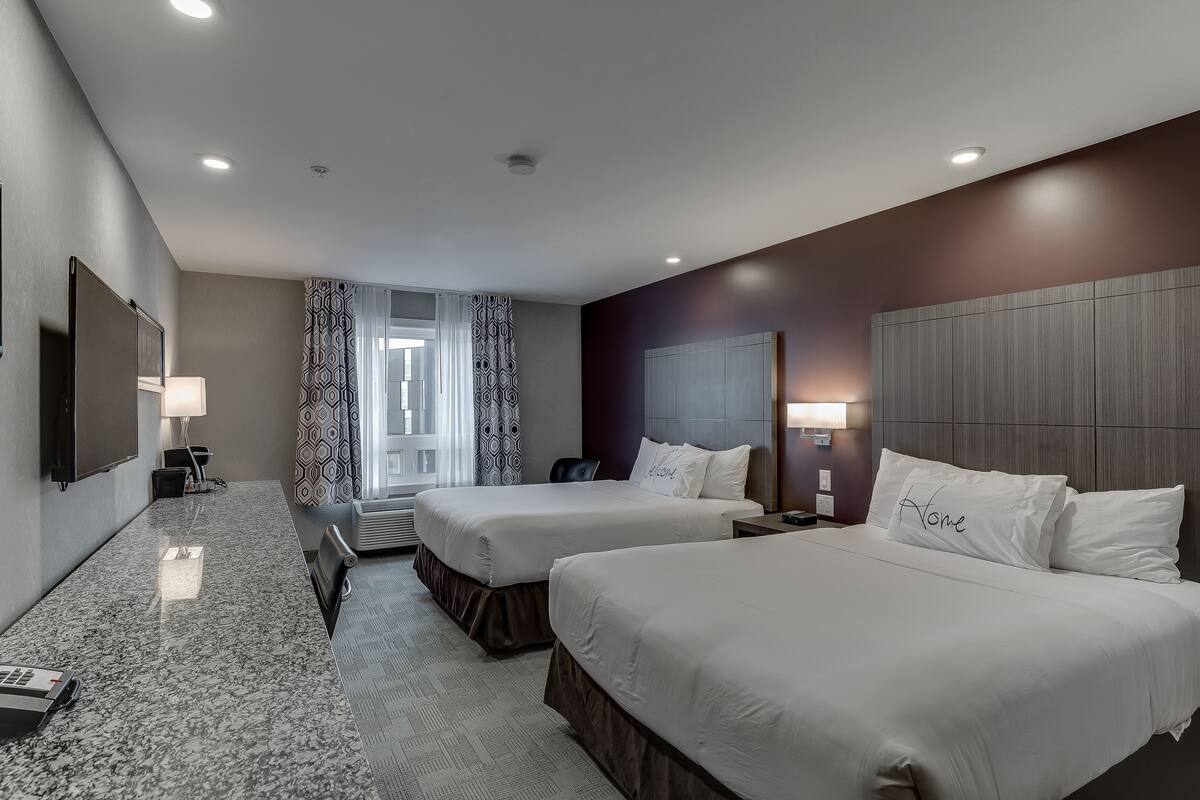 Une chambre d’hôtel avec deux lits, un bureau, une télévision et une fenêtre avec des rideaux à motifs.