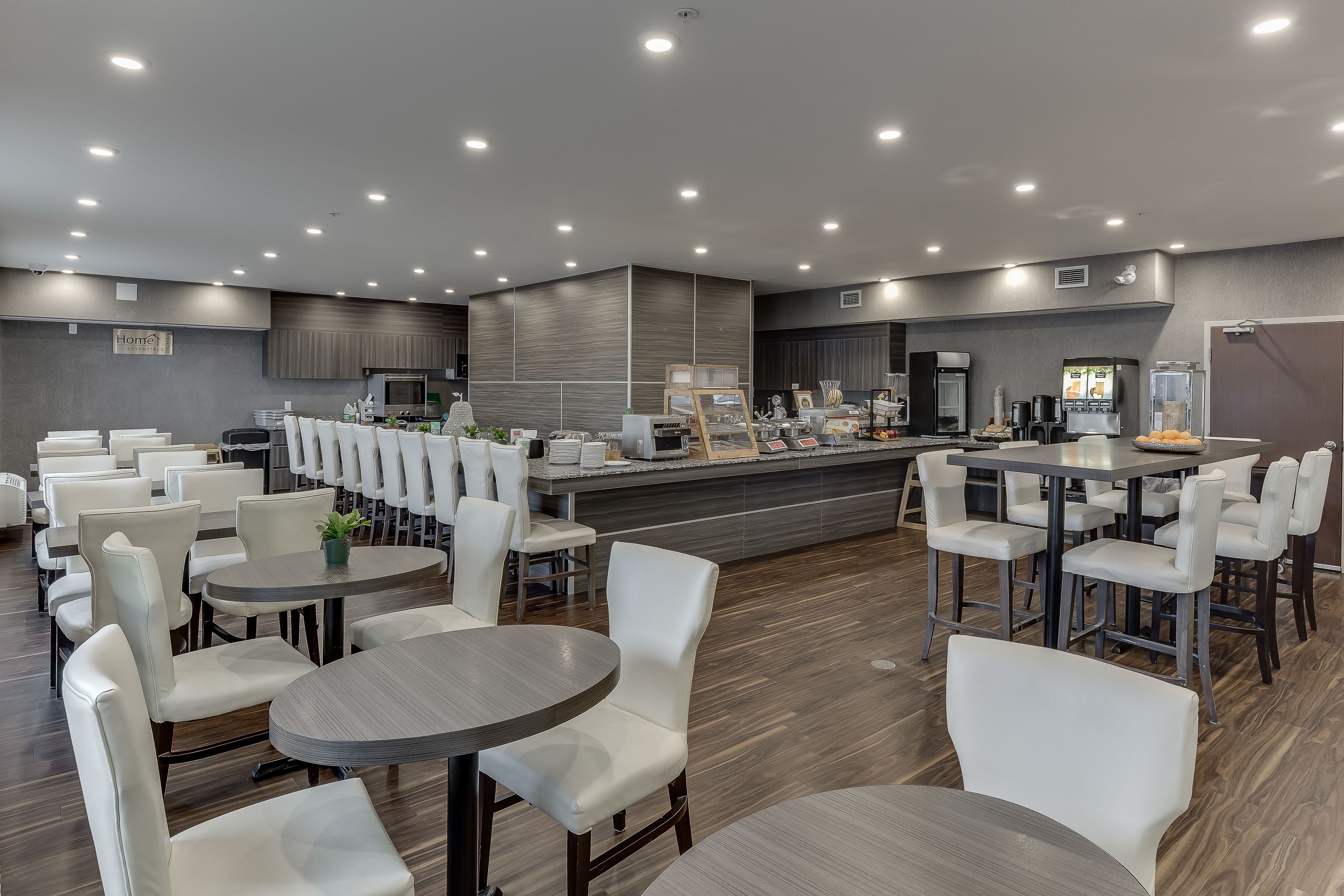 A modern restaurant with round tables and white chairs, a counter with a menu, and a kitchen in the background.
