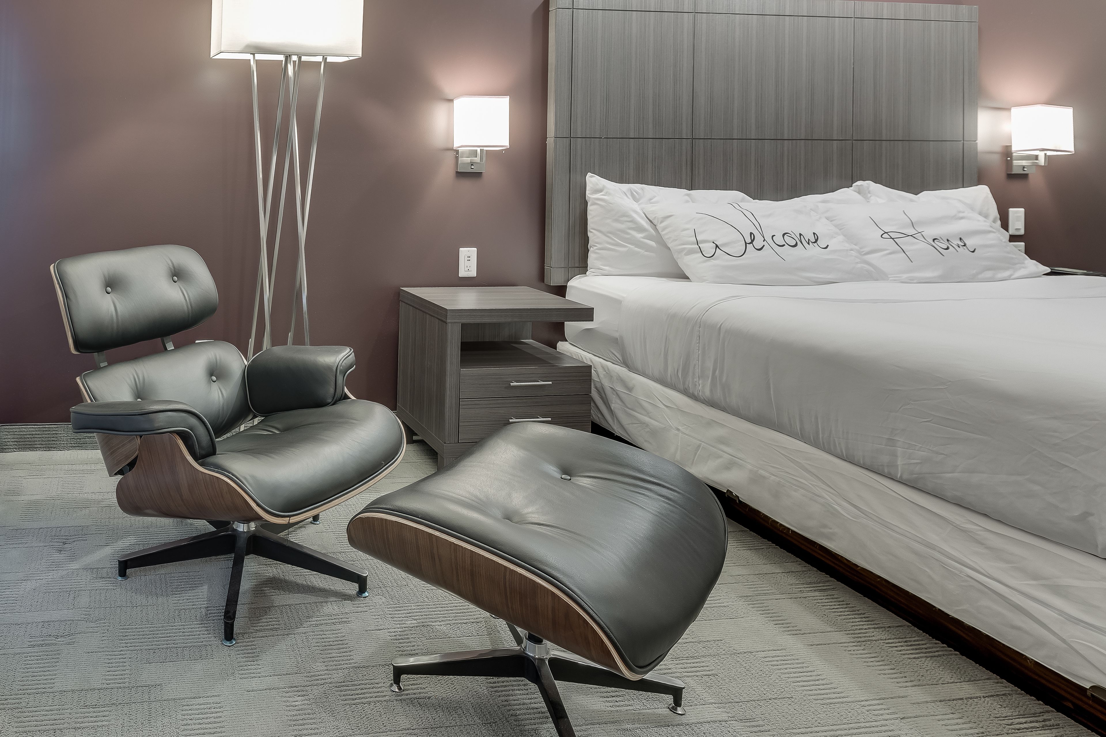 Quarto de hotel moderno com uma cama, escrivaninha, cadeira e uma mesinha.