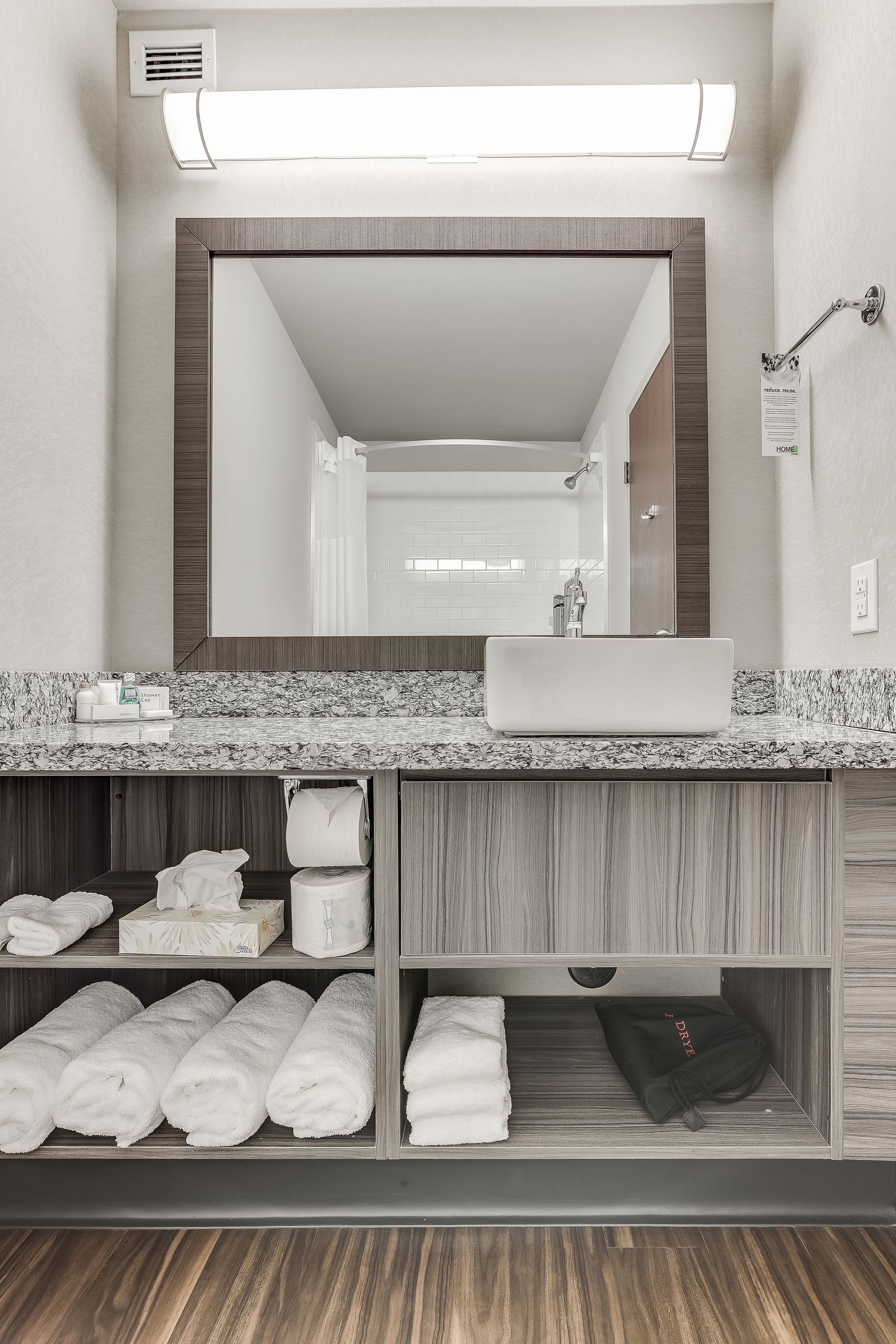 A modern bathroom with a large mirror, a sink, and a towel rack. There are towels and toiletries on the counter.
