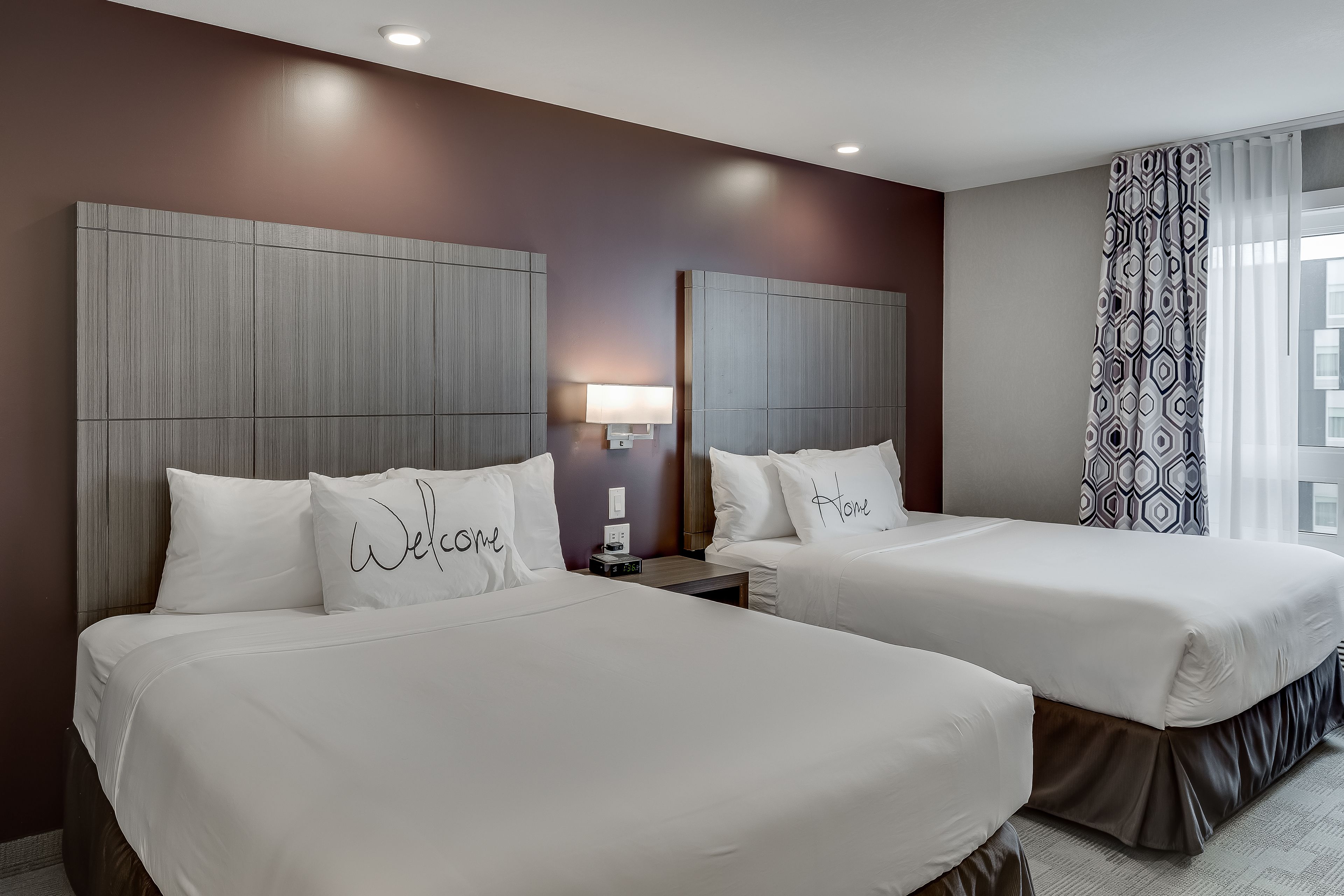 Una habitació d'hotel amb dos llits, cadascun amb un coixí que diu "Welcome" i "Home".