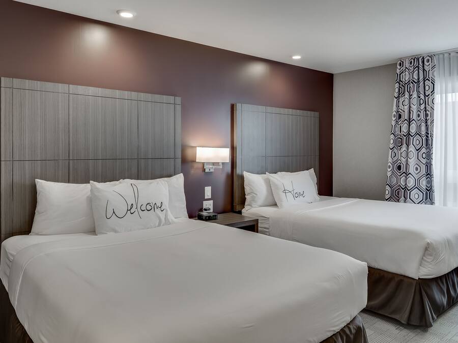 Una habitació d'hotel amb dos llits, cadascun amb un coixí que diu "Welcome" i "Home".
