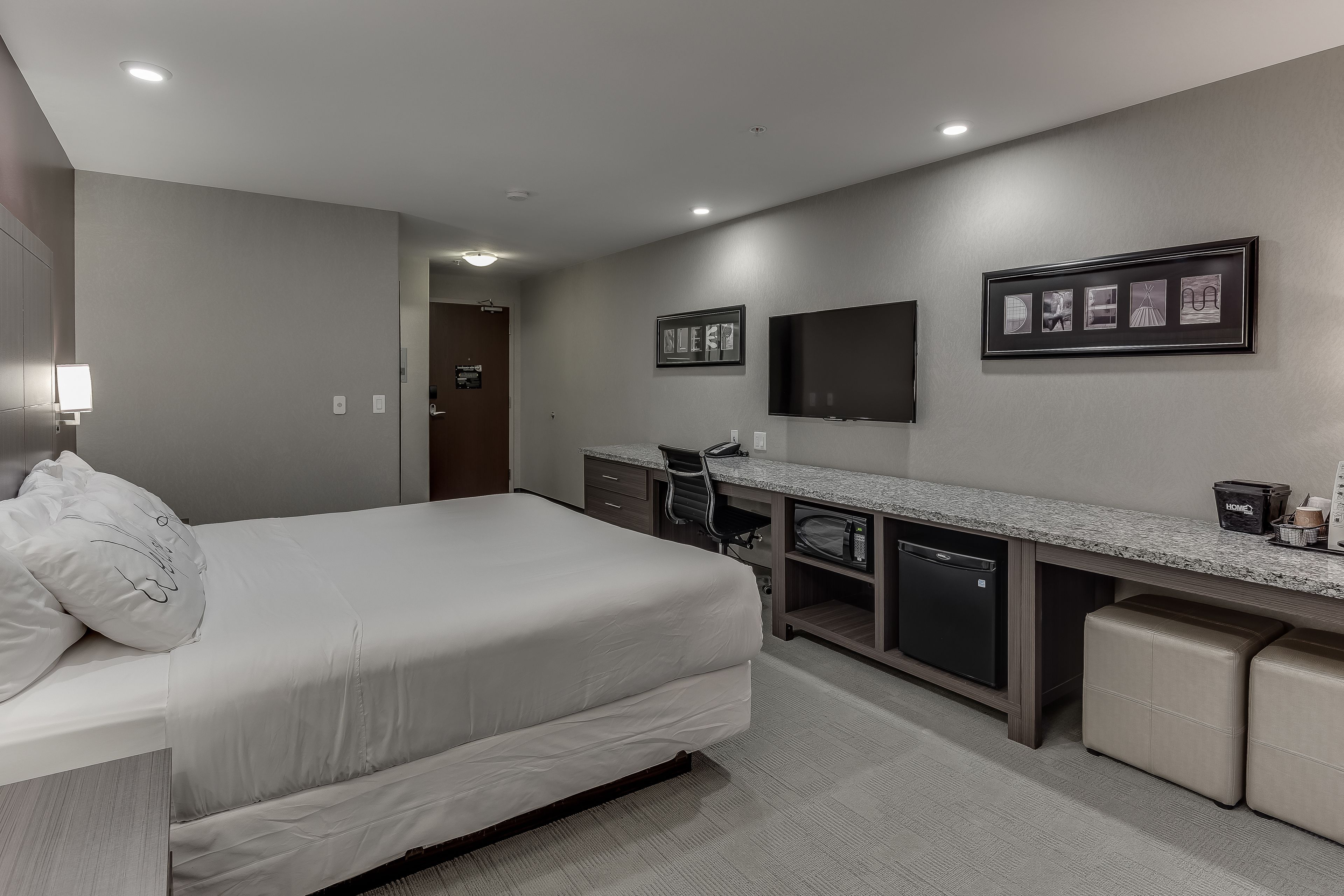 Une chambre d’hôtel moderne équipée d’un grand lit, d’un bureau avec une chaise, d’une télévision et d’un petit réfrigérateur.