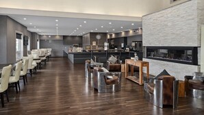 Un moderno hall de hotel con una larga recepción, zona de estar con sillones de cuero, chimenea y una cocina al fondo.