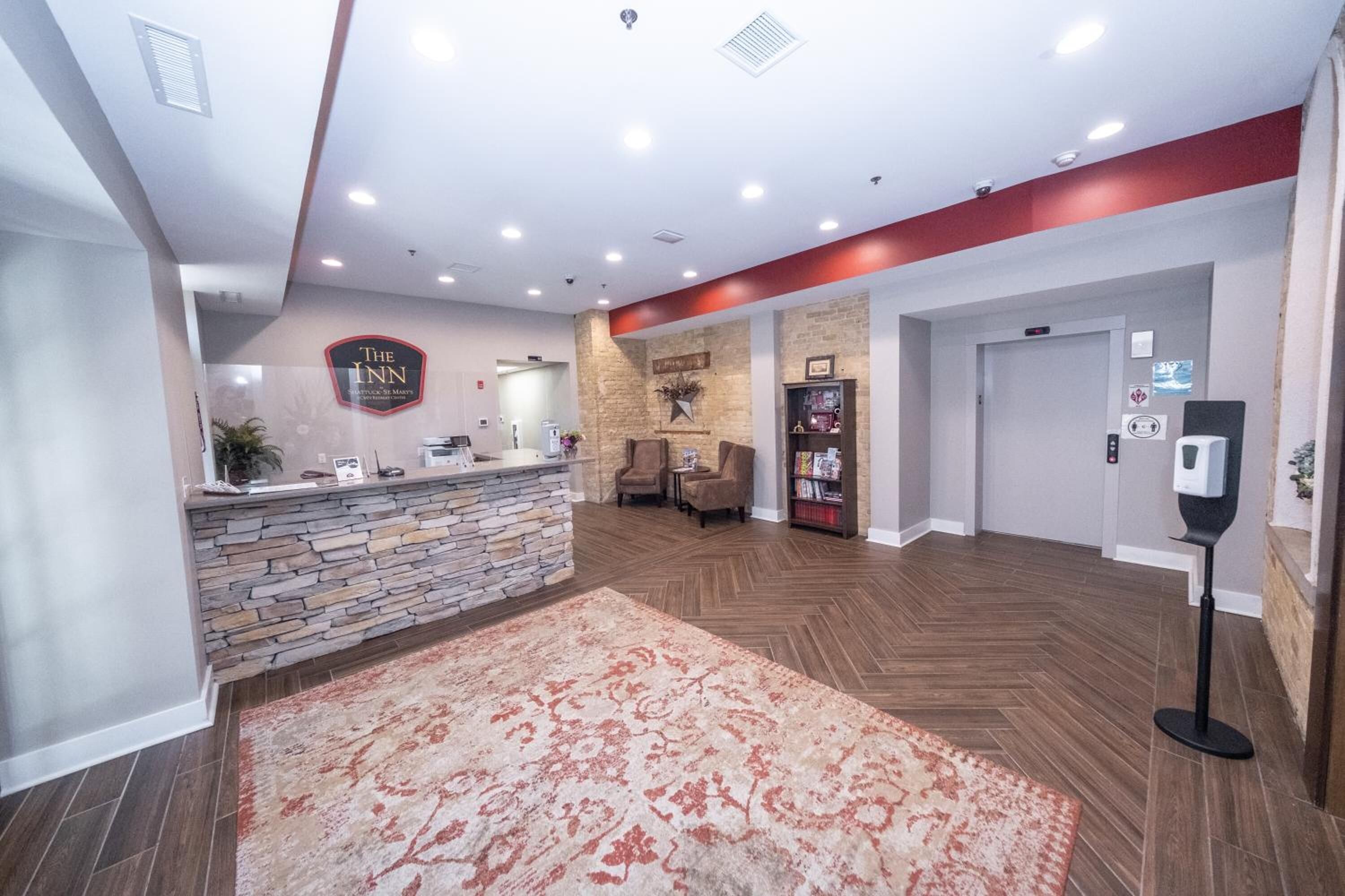 A hotel lobby with a reception desk, a stone wall, a fireplace, and a large rug.