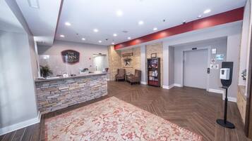A hotel lobby with a reception desk, a stone wall, a fireplace, and a large rug.